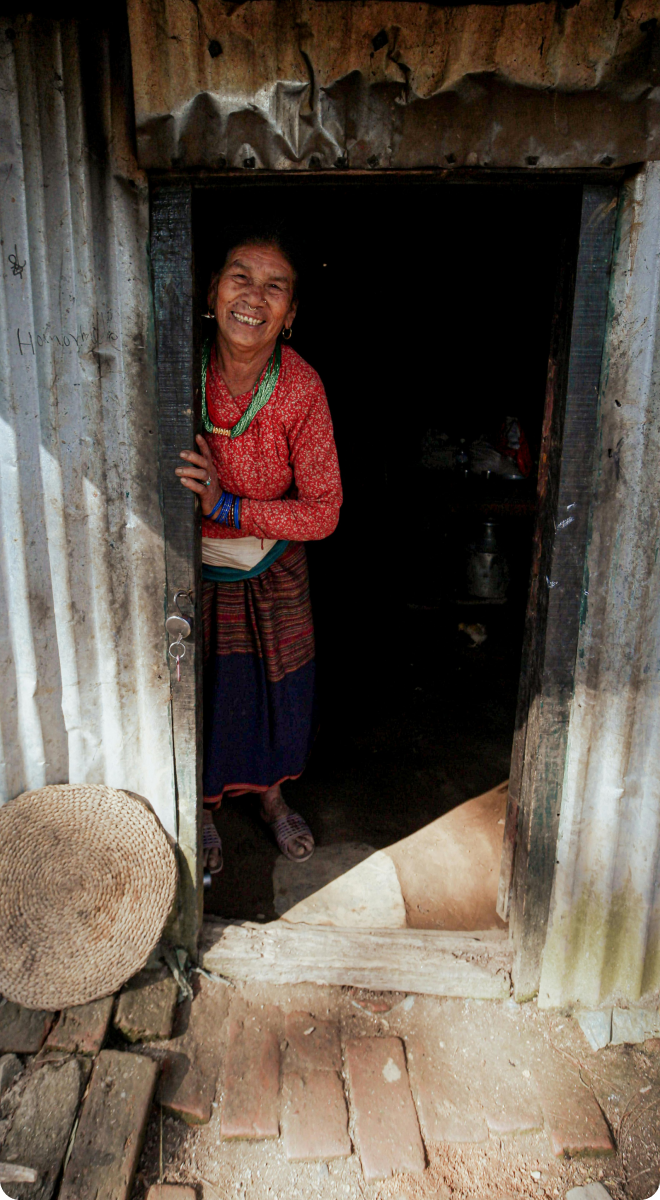 Smiling rural woman standing in doorway wearing traditional Nepalese dress